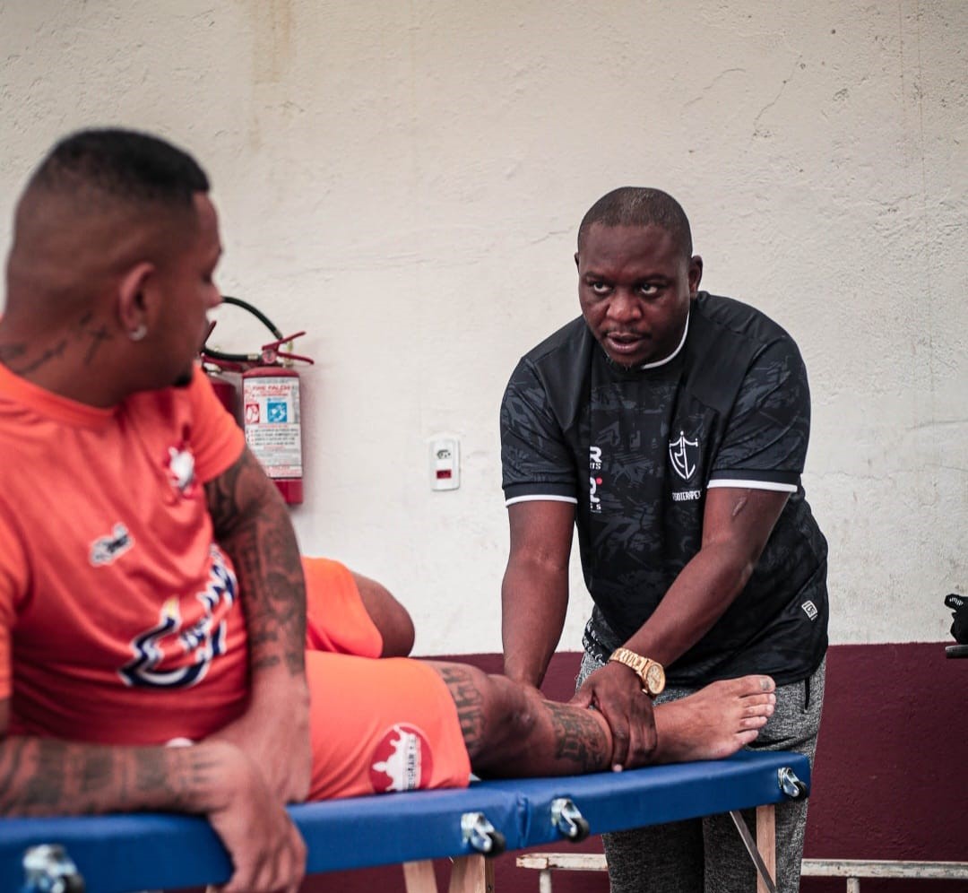 Fisioterapeuta atendendo atleta em maca durante sessão de fisioterapia esportiva
